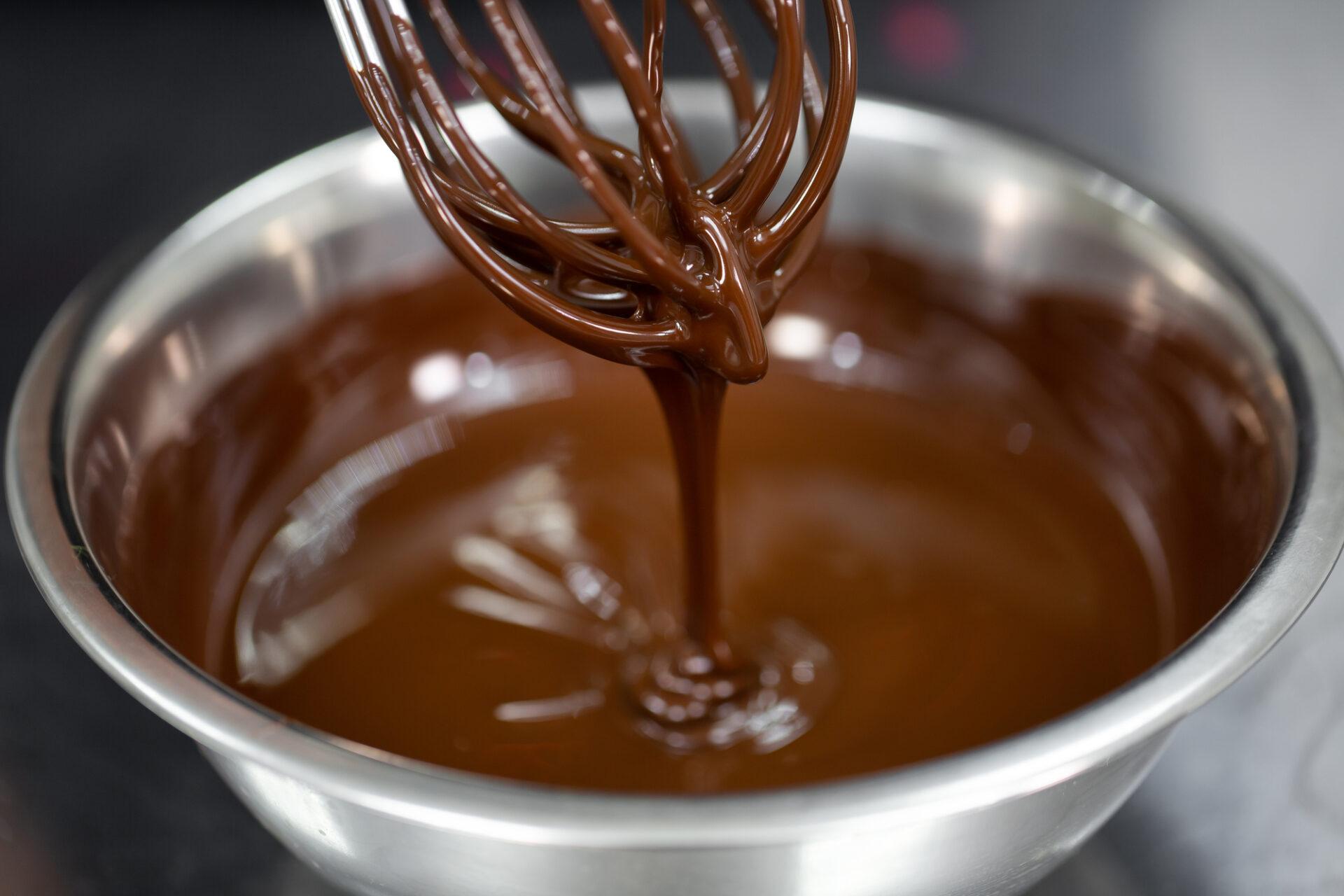 pastry chef whips melted chocolate in a bowl with a metal wire whisk close up.